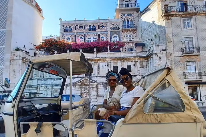 Guests relax in a tuk tuk in Lisbon historic center, with ornate facades on a 3-hour private tour