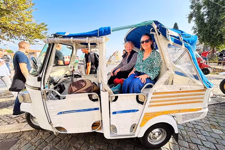 Guests seated in a tuk tuk on a 3-hour private tour of Lisbon’s historic center, sunny city sightseeing