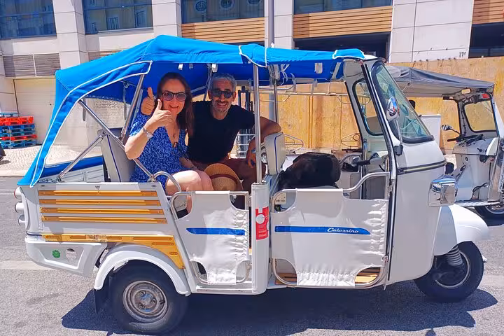 Couple smiling in blue-roof tuk tuk on Lisbon 3-hour private historic center tour, ready to explore