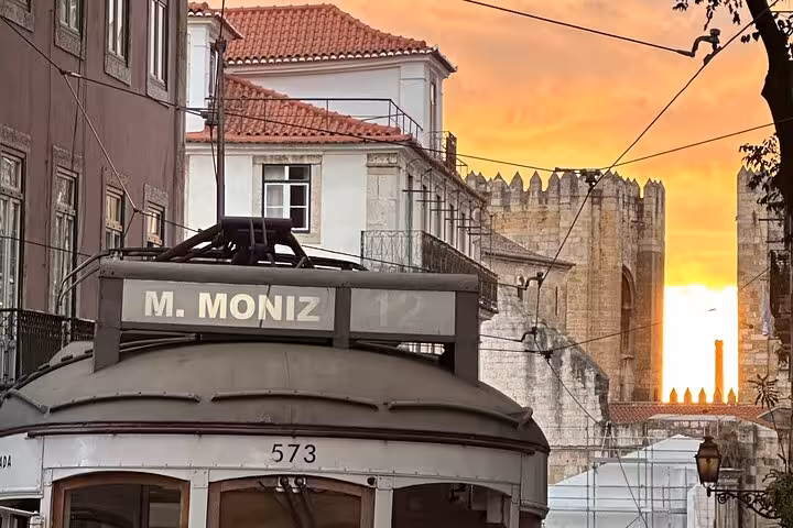 Historic Lisbon tram passing through Alfama district at sunset, showcasing iconic architecture.