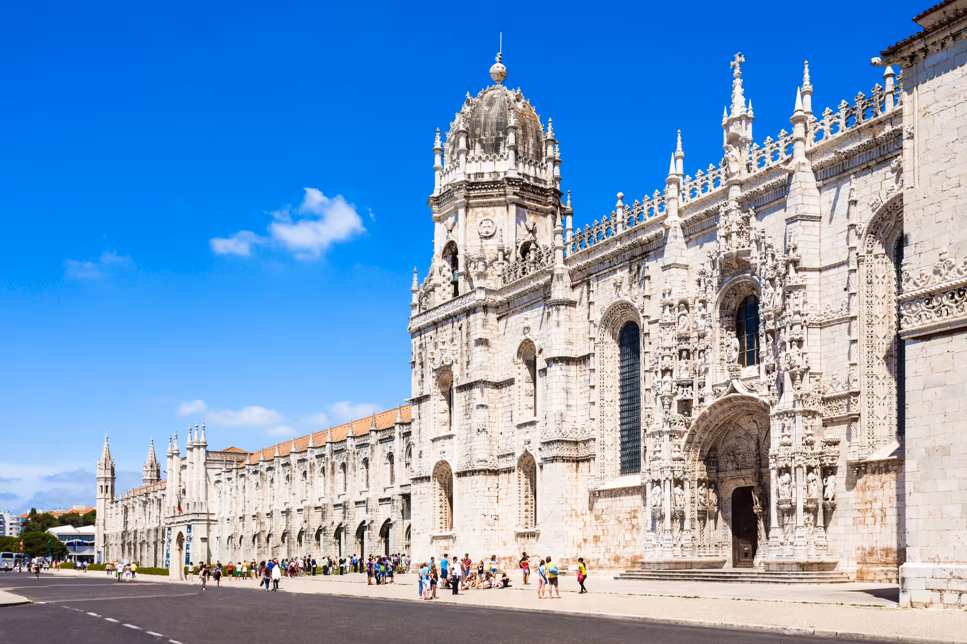 Visitors admire the stunning architecture of Jerónimos Monastery in Lisbon on a clear day.
