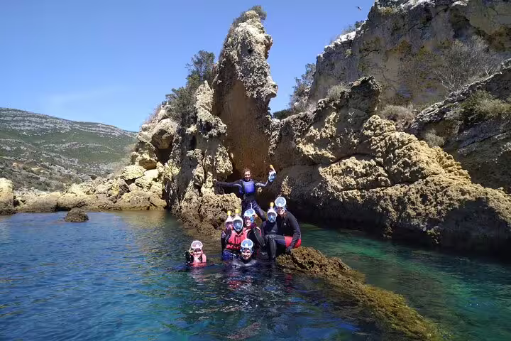Group of adventurers in wetsuits explore rocky coastal waters on a Lisbon kayaking and coasteering adventure.
