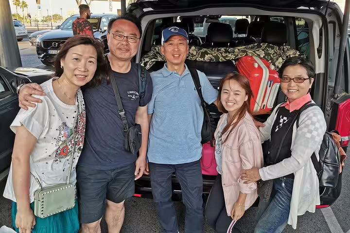 Group of travelers pose by a car during a Lisbon to Madrid private transfer with scenic stops in Evora and Toledo.