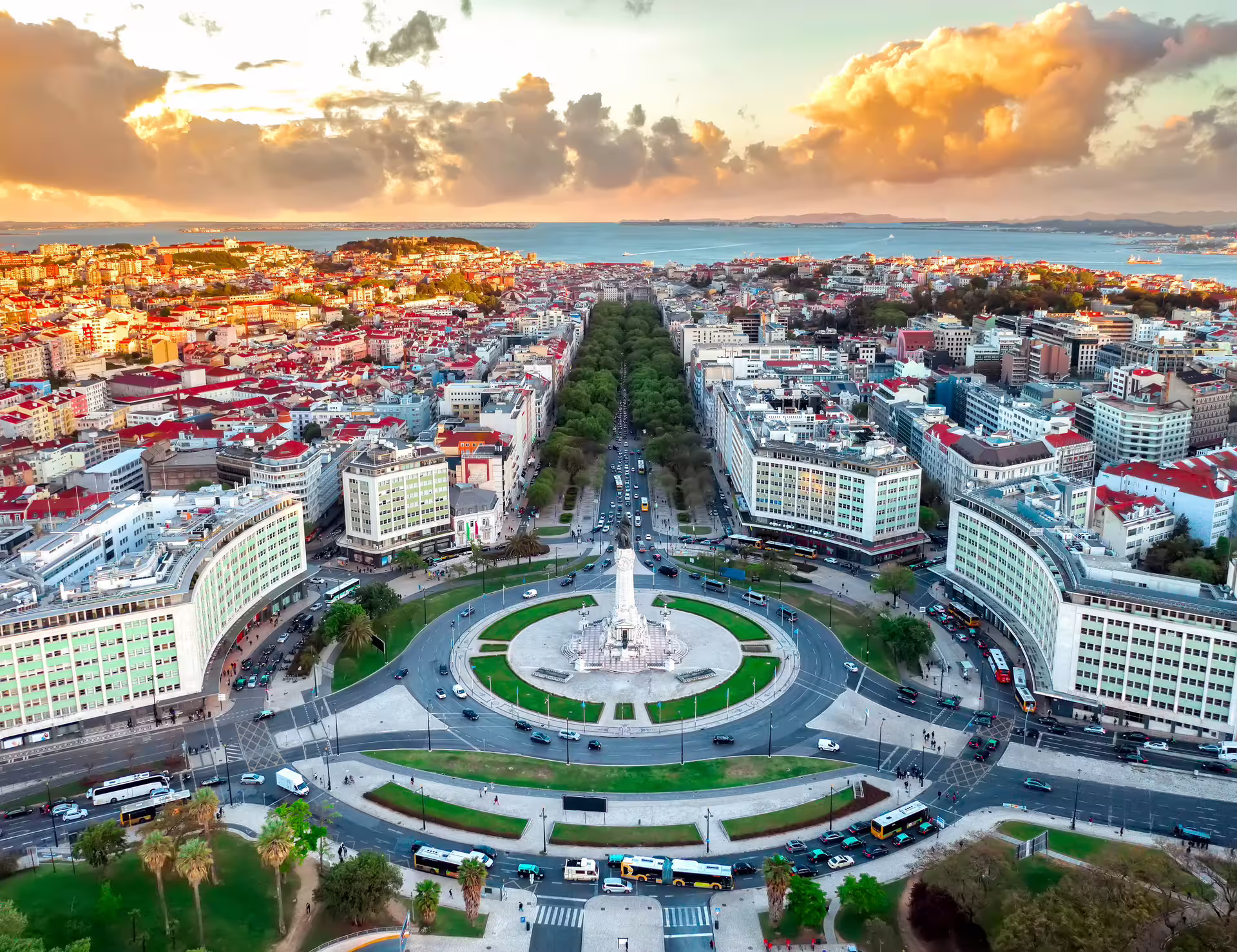 Aerial view of Lisbon's historic Marques de Pombal Square, surrounded by vibrant cityscape and sunset-lit sky.