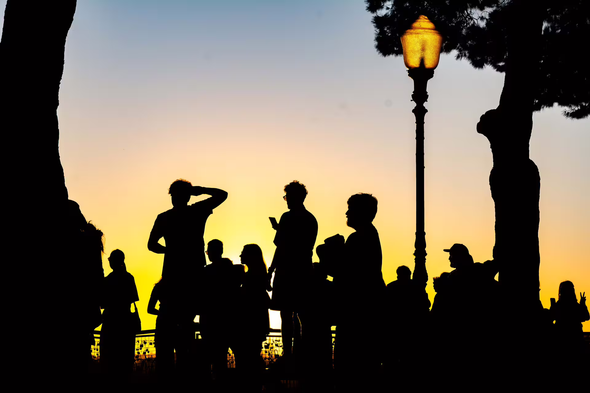 Silhouetted group under Lisbon streetlight against sunset sky, capturing festive magic on a Christmas lights photo walk.