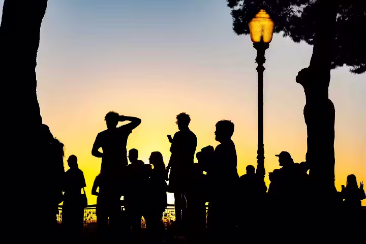 Silhouetted group enjoys Lisbon cityscape during private sunset and night photo walk, framed by a glowing streetlamp and trees.