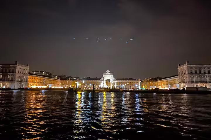 Lisbon's Praça do Comércio illuminated at night, reflecting vibrant lights on the Tagus River during a sailing tour.