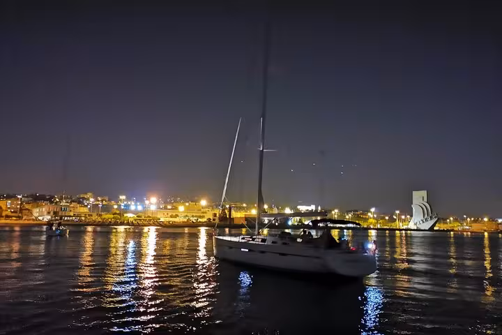 Sailboat cruising the Tagus River at night in Lisbon, city lights reflecting, drinks included on board
