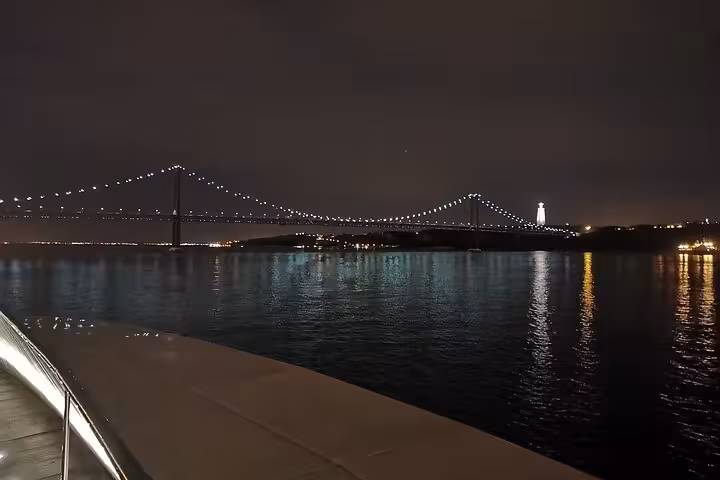25 de Abril Bridge lit up at night over the Tagus River, scenic Lisbon night sailing tour with drinks included