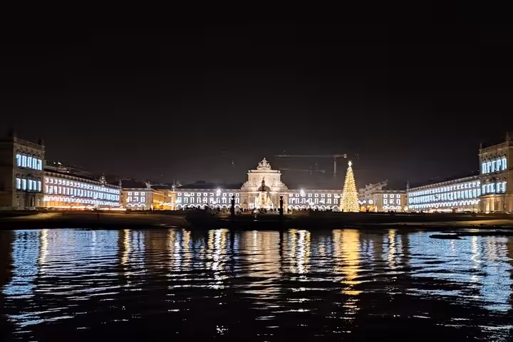 Night sailing tour view of Lisbon's Praça do Comércio lights reflecting on the Tagus River with onboard drinks