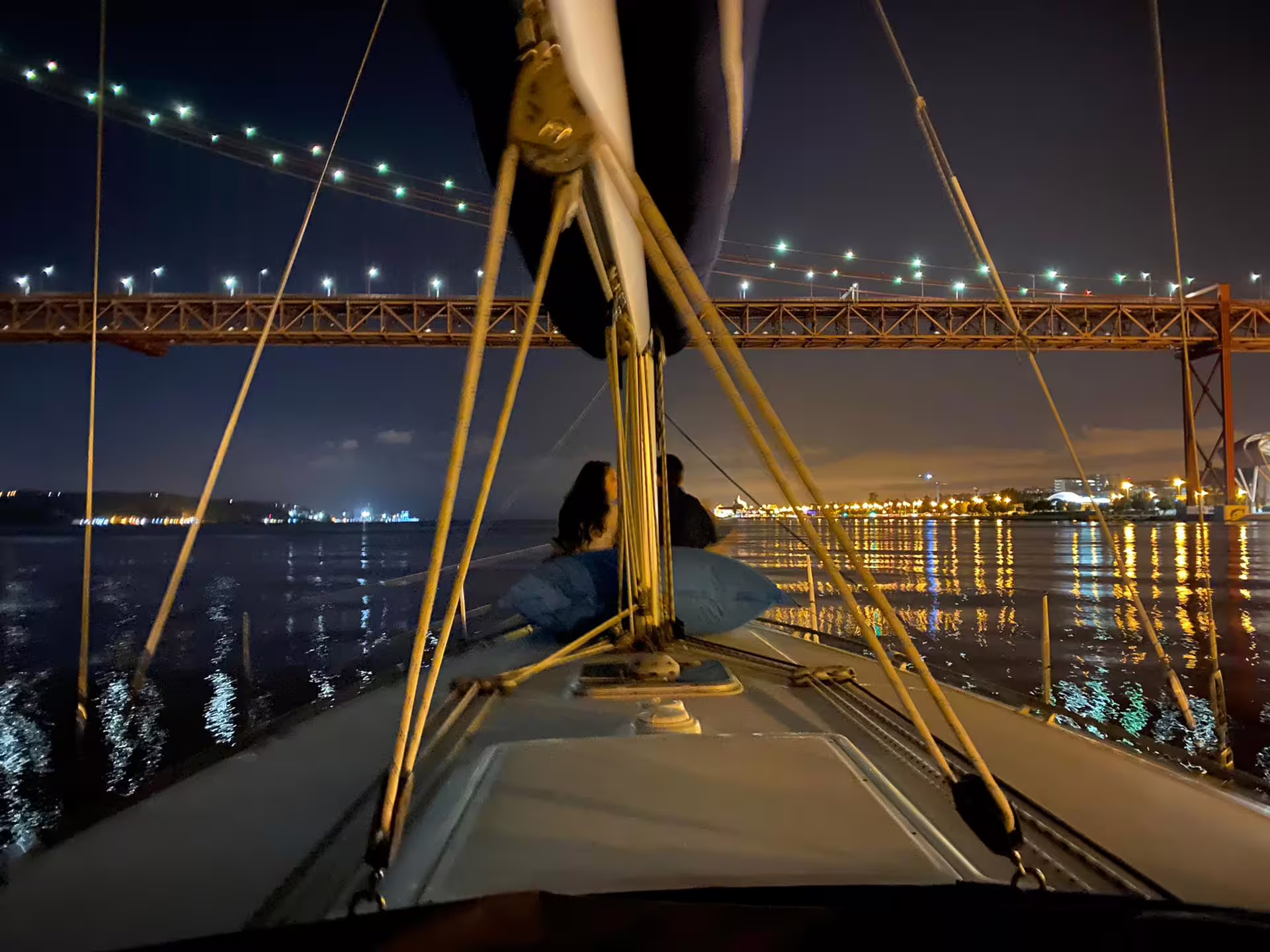 Sailing under the lit-up Lisbon bridge at night, offering stunning views and a unique tour experience.
