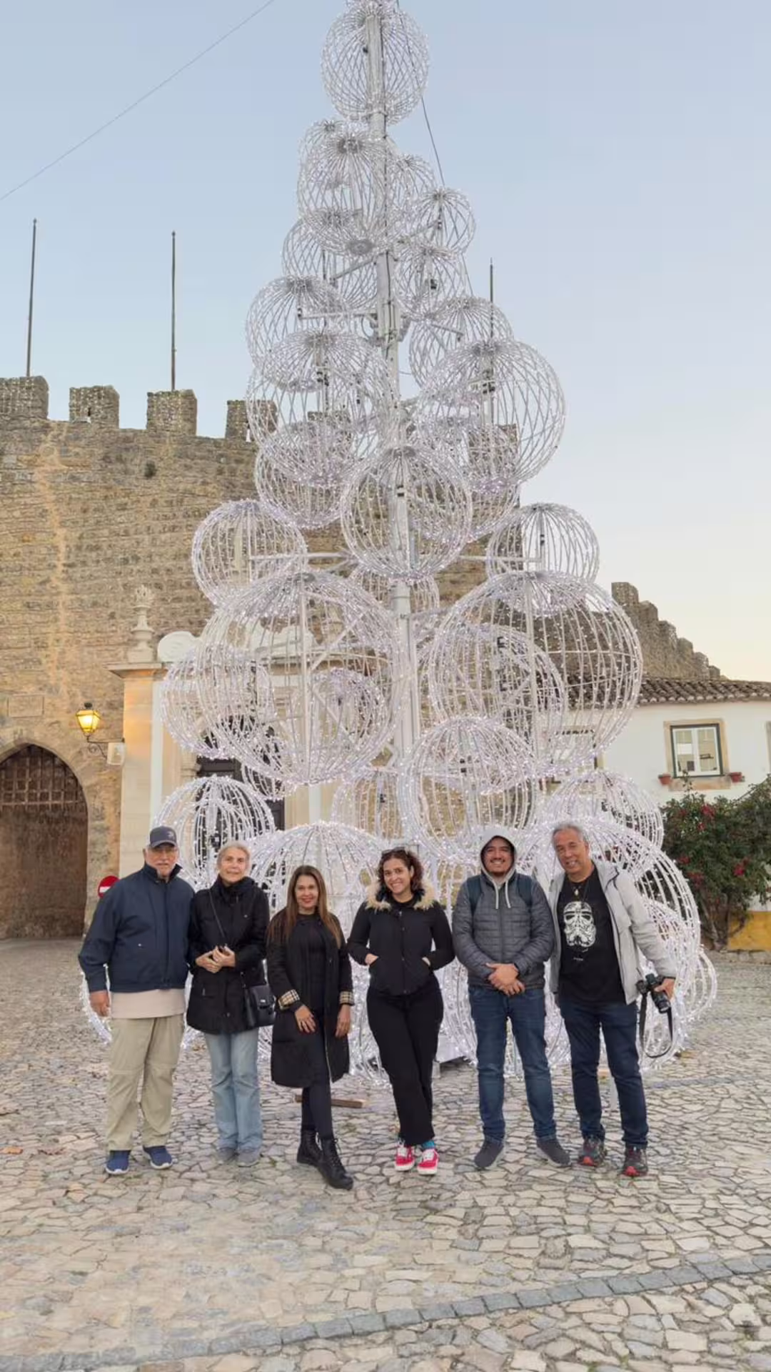 Group of tourists in Óbidos posing in front of a festive light sculpture on a guided tour from Lisbon.
