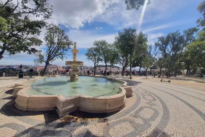 Scenic view of a historic fountain surrounded by trees and intricate stone pavement in Lisbon’s Old Town, perfect for a private half-day tour.