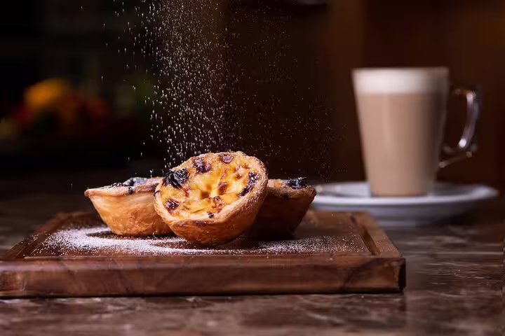 Delight in Lisbon's culinary journey with traditional pastéis de nata, dusted with sugar, paired with a creamy coffee backdrop.