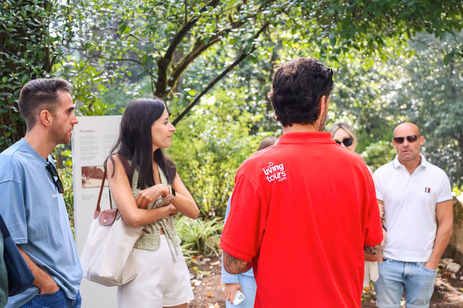 Tour guide in red shirt leading a small group through lush greenery, part of a guided tour to Pena Palace.