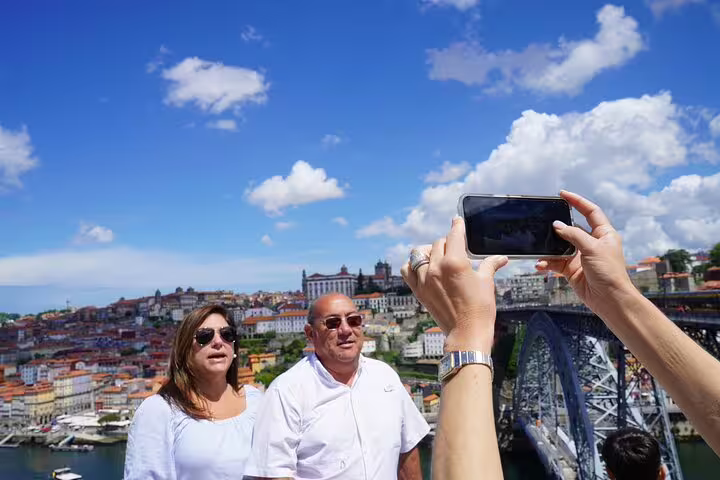 Tourists enjoy a scenic view of Porto's skyline and the Dom Luís I Bridge on a sunny day during a 3-day Lisbon to Douro Valley tour.