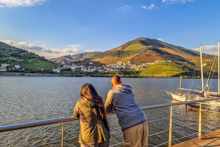 Travelers enjoying Douro River views on Lisbon to Porto ride, with vineyard hills and boat in the valley