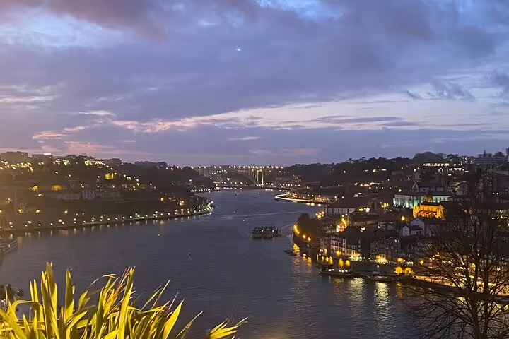 Twilight over Porto's illuminated riverbanks and bridges, an enchanting sight for travelers on a Lisbon to Porto private transfer.