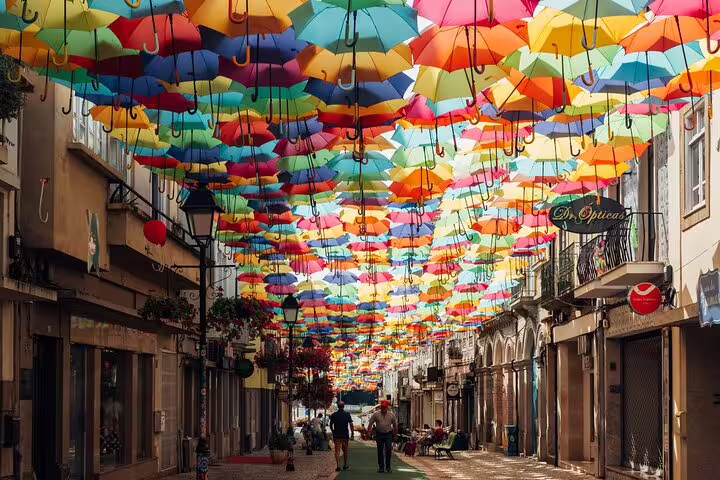 Vibrant umbrellas float above a bustling street in Águeda, Portugal, perfect for a Lisbon to Porto transfer tour stop.
