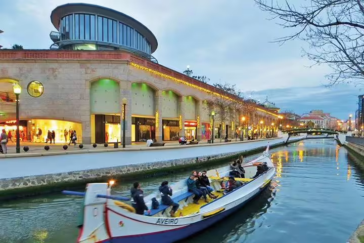 Scenic boat tour on Aveiro canal with lit shopping mall, part of Lisbon to Porto transfer stopping in Aveiro.