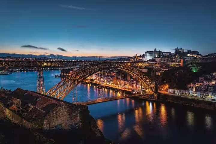 Stunning night view of Porto's Dom Luís I Bridge illuminated over the Douro River, perfect for scenic stops on a Lisbon to Porto transfer.
