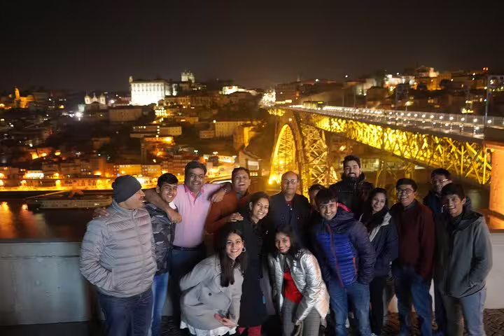 Group enjoying a scenic night view of Porto with the illuminated Dom Luís I Bridge, part of Lisbon to Porto transfer tour.