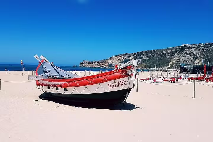 Traditional fishing boat on Nazaré's sandy beach under clear skies, popular stop on Lisbon to Porto private transfer.