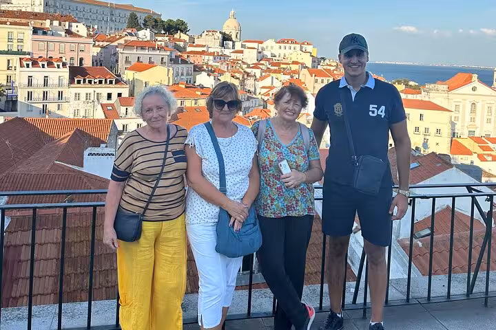 Group of tourists posing at a Lisbon viewpoint with panoramic views of the historic Alfama district.