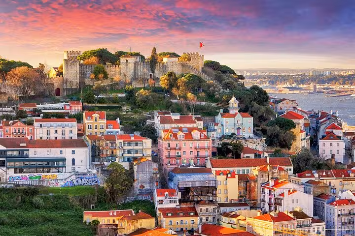Colorful historic buildings and St. George's Castle under a vibrant sunset on a Lisbon private tour.