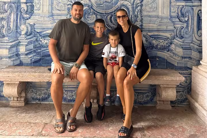 Family enjoying a Lisbon private tour, seated on a bench with intricate blue azulejo tiles in the background.