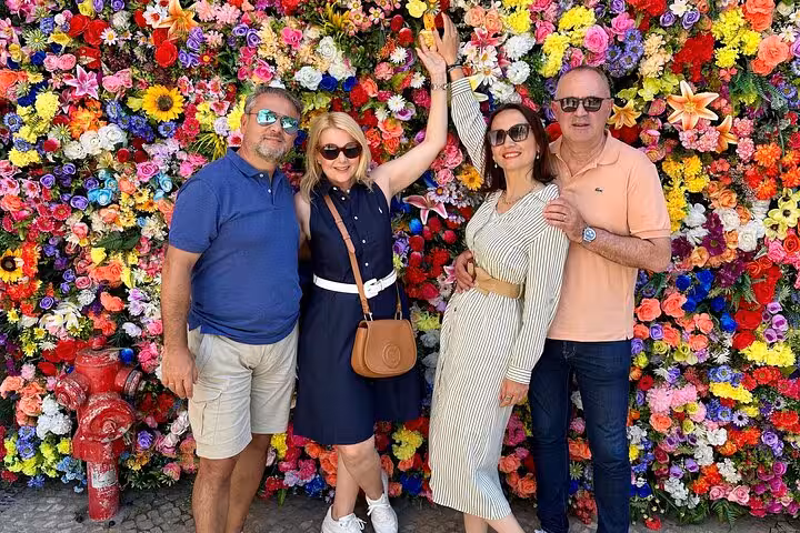 Four friends posing joyfully in front of a vibrant flower wall in Lisbon on a private city tour.