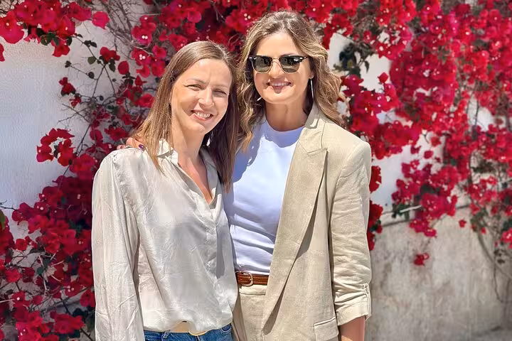 Two women smiling in front of vibrant bougainvillea during a Lisbon private tour, showcasing local charm and beauty.