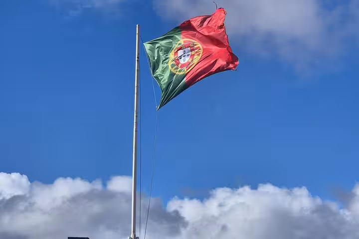 Portuguese flag waving against a bright blue sky, symbolizing Lisbon's rich cultural heritage.