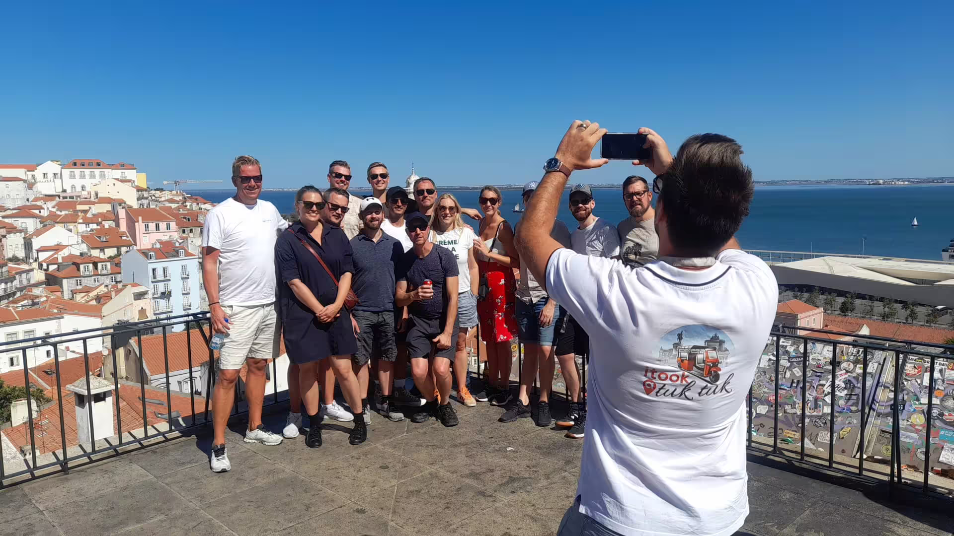 Group enjoying Lisbon's scenic viewpoint on a private tuk tuk tour with stunning city and ocean backdrop.