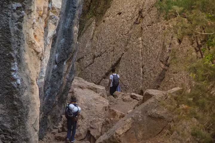 Adventurers traverse narrow rocky passage on Lisbon climbing tour, showcasing dramatic rock formations and gear.