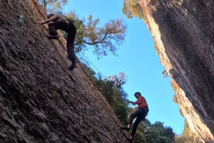 Climbers scaling steep rock walls under blue skies on Lisbon full day climb adventure trail.
