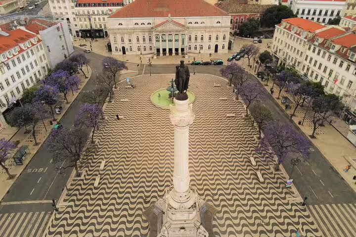 Aerial view of Lisbon's Rossio Square with iconic wave-patterned pavement, vibrant jacaranda trees, and historical architecture.