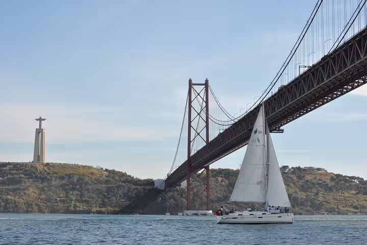 Sailboat passing under 25 de Abril Bridge with Cristo Rei, Lisbon 2-hour small group Tagus River sailing cruise