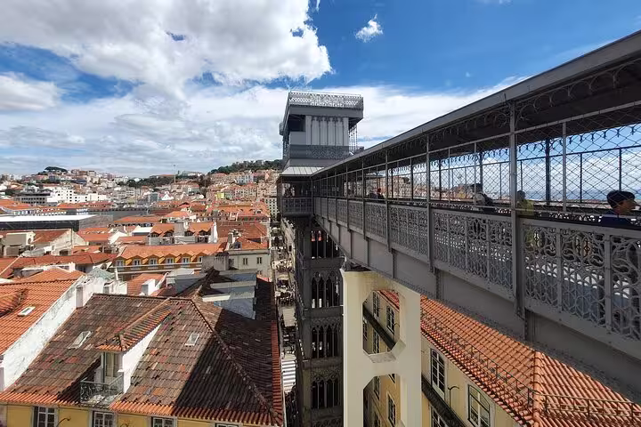View of Lisbon's iconic Santa Justa Lift with red-tiled rooftops and a clear blue sky, featured on a small-group tour.