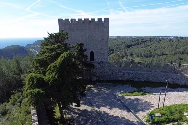 Historic stone castle tower surrounded by lush greenery and ocean views near Sesimbra.