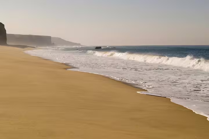 Golden sandy beach with gentle waves and scenic cliffs on the Setúbal Peninsula, ideal for a Lisbon to Setúbal half-day tour.