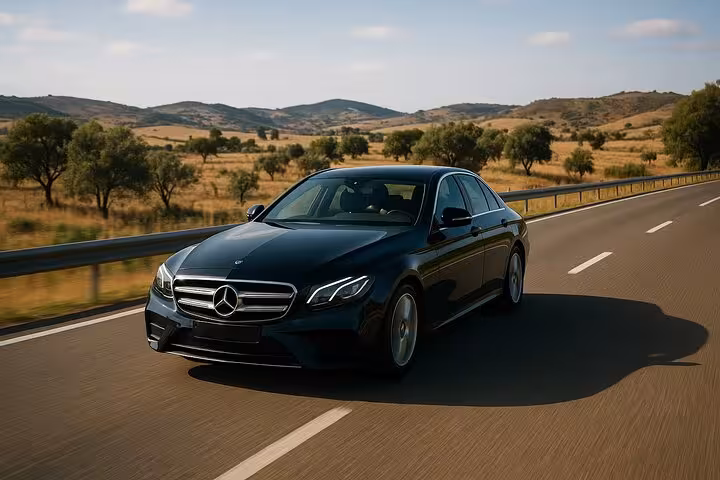 Luxury black Mercedes driving through scenic countryside on Lisbon to Seville private transfer route.