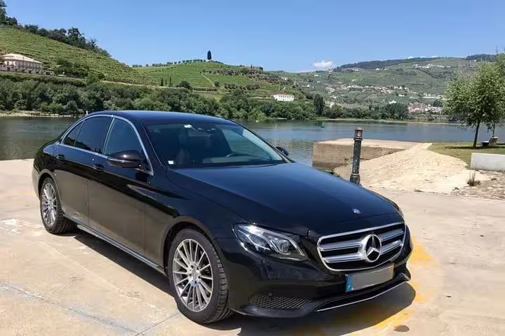 Luxurious black Mercedes sedan parked by a scenic river, ideal for Lisbon to Seville private journey on direct route.