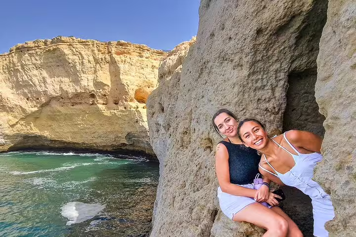 Two smiling women enjoy scenic cliffs and turquoise sea views in the Algarve during a Lisbon to Seville private transfer tour.
