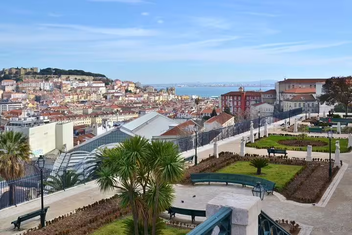 Scenic Lisbon cityscape from a garden terrace, showcasing historic architecture and the Tagus River in the background.