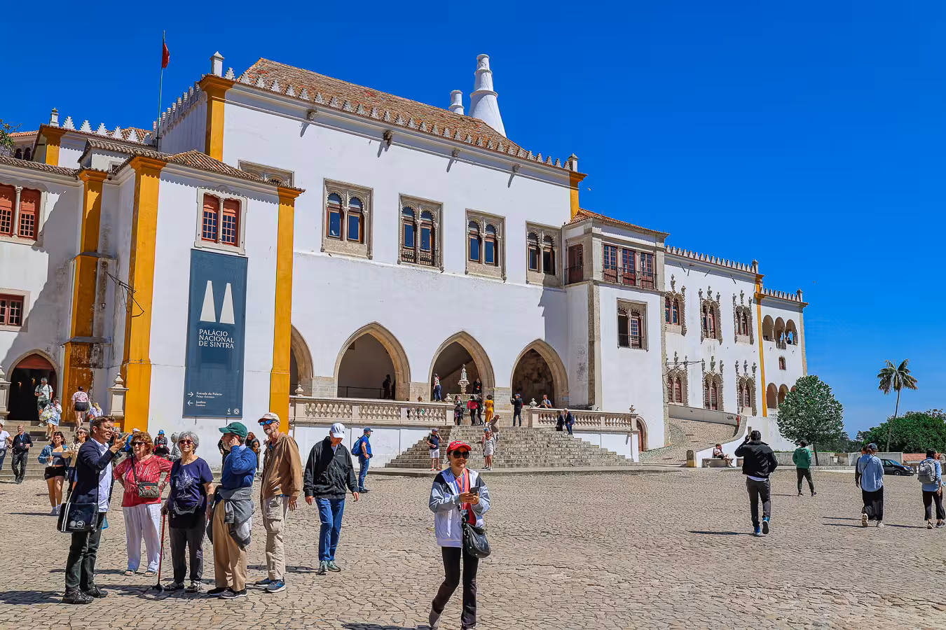Visitors explore the historic Palácio Nacional de Sintra under a clear blue sky on a guided tour from Lisbon.