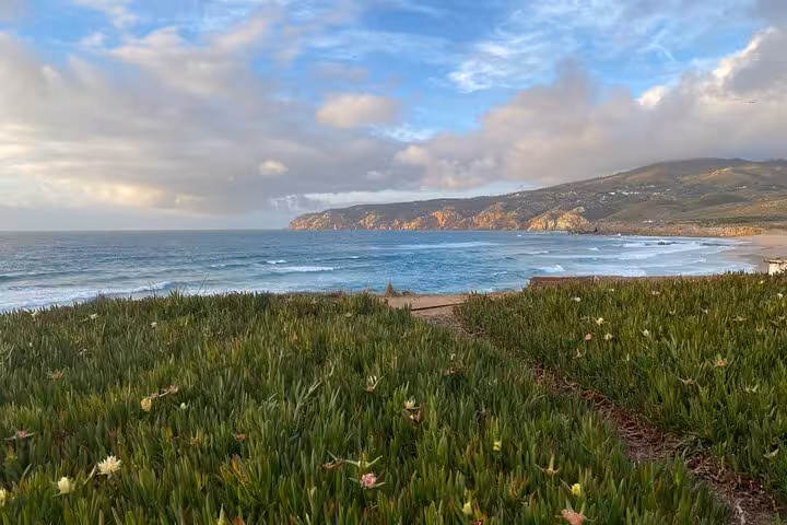 Scenic view of the rugged coastline near Sintra, with lush greenery and waves crashing under a vibrant sky.