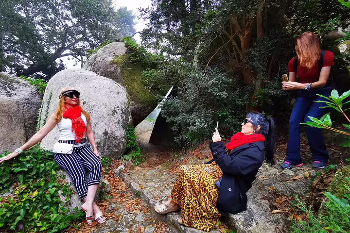 Tourists explore scenic rock formations in Sintra's lush greenery during a private 2-day Lisbon and Cascais adventure.