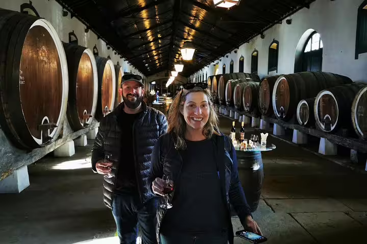 Tourists enjoying a wine tasting experience in a rustic Lisbon cellar, part of a private two-day tour through Lisbon, Sintra, Roca, and Cascais.
