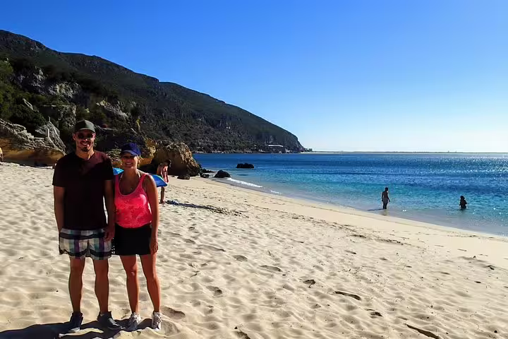 Couple enjoys sunny beach with clear blue waters and scenic cliffs during Lisbon's South Sights & Wine tour getaway.
